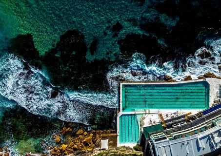 A aerial shot of a swimming pool along a rocky coastline in Sidney, Australia. The turquoise water