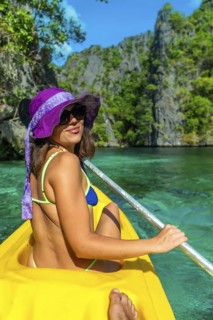 Young woman paddling a yellow kayak in the turquoise waters of twin lagoon, coron island, enjoying