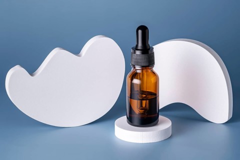 A single cosmetic serum bottle with a dropper, elegantly placed on a round white podium against a