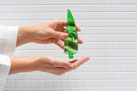 Cropped unrecognizable woman applying aloe vera gel from a green bottle onto her hand against a