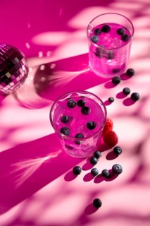 A vibrant pink backdrop highlights two glasses filled with a refreshing pink drink, garnished with