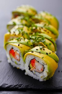A close-up view of a sushi roll topped with slices of fresh avocado, sprinkled with sesame seeds,
