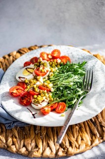 A vibrant keto lunch featuring boiled eggs, fresh rocket, cherry tomatoes, canned green peas, and