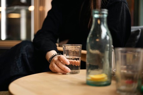 Cropped unrecognizable girl holding a glass of water at a cafe table, with a bottle beside her and