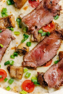 Close-up view of mozzarella pizza topped with roast beef, porcini mushrooms, cherry tomatoes, and