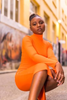 Fashionable urban style with a black African girl in an orange dress and black heels on a city