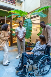 Happy diverse coworkers chatting at the entrance of the office with a disabled woman with