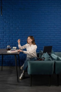 A woman wearing casual clothes works remotely in a cozy cafe. With a laptop, books, and tea, she is