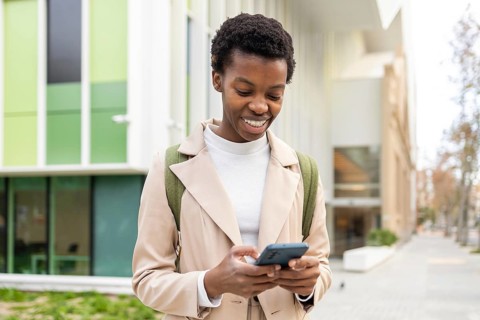 Smiling black woman using her smartphone in an urban setting, showcasing modern lifestyle and
