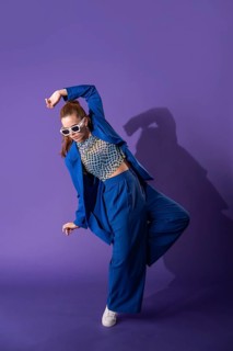A young woman dancer striking a dynamic pose against a vivid purple background. Her contemporary