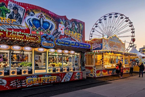 Colourful carousel stands and an illuminated Ferris wheel at dusk at a fair, carousel and the