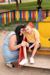 Mother and son with cerebral palsy share a tender moment at a colorful playground. Smiling and