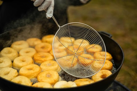 Cropped unrecognizable cook prepares doughnuts in a hot oil pan at a street fair, skillfully using