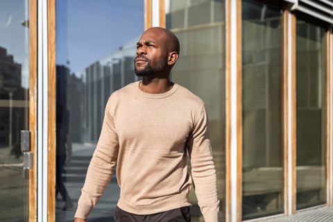 A cuban man strides confidently outside, basking in sunlight next to a modern glass structure. His
