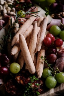 A close-up of crunchy breadsticks surrounded by a colorful assortment of fresh grapes, thinly