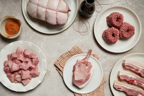 A rustic display of fresh meat cuts, including a roast, minced meat, ribs, chops, and diced pieces,
