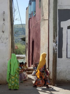 Women in colorful hijabs and children walk through a sunny alley, Harar, Ethiopia