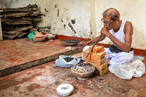Man focuses on starting coal fire with a blowpipe, a man burns safire in a small stove in the city