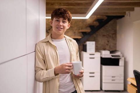 Young man enjoying a coffee break in a modern coworking space, standing relaxed with a cup. The
