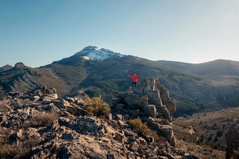 Back view of unrecognizable male hiker with arms wide open on a rock, celebrating his climb at the