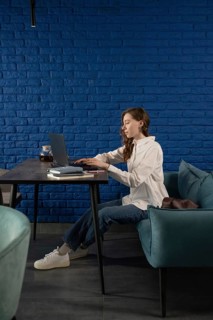 A woman sits in a modern blue cafe, working on a laptop at a black table. She is focused, wearing a