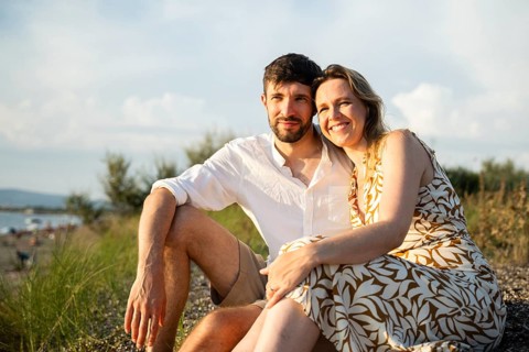 A couple enjoys a sunny day at the Italian beach, sitting on the sand with a backdrop of the sea