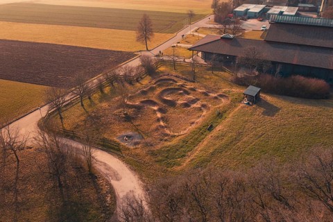 Ground area with curvy contours near a building, surrounded by quiet rural landscape, bike park,