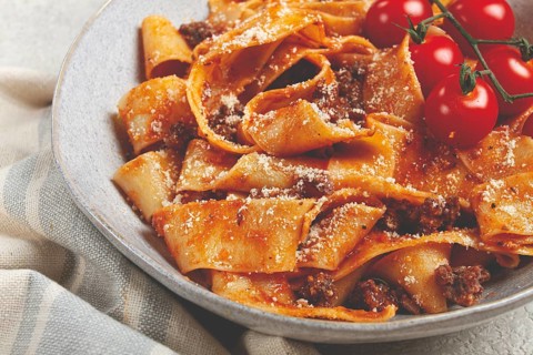 Pappardelle pasta with bolognese sauce, topped with parmesan cheese and cherry branch, homemade, no