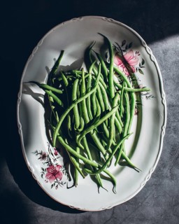 A cluster of green beans arranged elegantly on a vintage floral porcelain plate, capturing the
