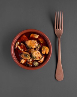 Top view of a ceramic bowl filled with cooked mussels served in a savory sauce, accompanied by a