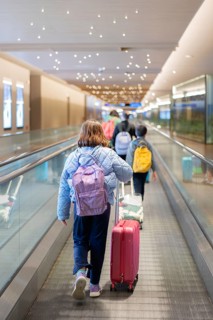A family with children walks through a modern airport terminal. They are on a moving walkway,