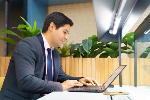 A young Chilean businessman in a modern suit focuses on his laptop in a contemporary setting,