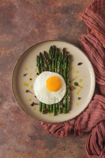 Grilled asparagus, with fried egg, spices and herbs, parmesan cheese, on a beige plate, top view,
