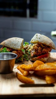 A delicious crispy chicken sandwich with fresh lettuce and tomatoes served on a wooden board.