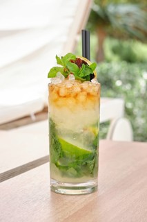 A vibrant mojito cocktail sits on a wooden table, topped with fresh mint leaves and lime slices.