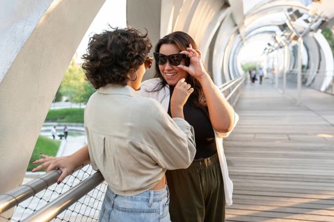 A joyful lesbian couple shares a playful moment on a modern, arched bridge. Their connection is