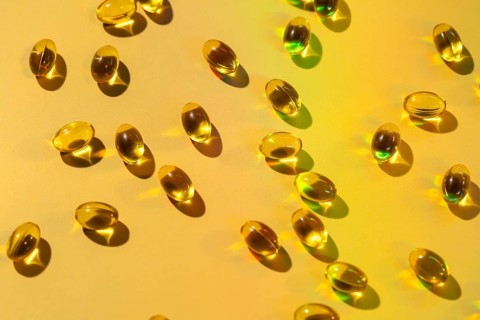 A collection of glossy softgel capsules scattered on a vibrant surface, highlighting their use as