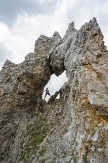 Mountaineer with helmet standing in a rock arch, ascent to the Maukspitze, clouds moving around the