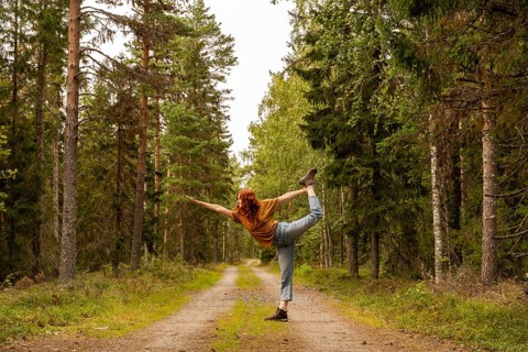 A woman performs a yoga pose on a forest path lined with lush trees in Sweden, embodying balance