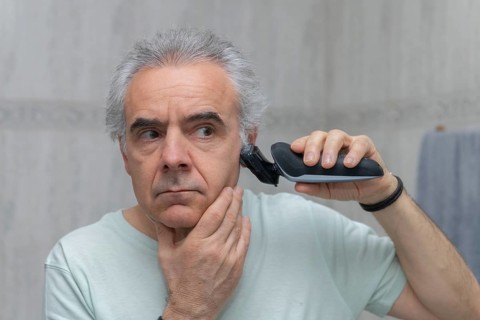 Mature man using an electric clipper for a home haircut. Focused on achieving a neat appearance and