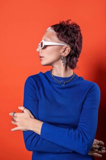 A fashionable young woman in a vivid blue top stands against an orange background, showcasing her