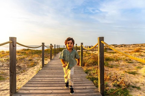 Young boy walking towards the viewer on a wooden boardwalk, smiling and enjoying summer holidays in