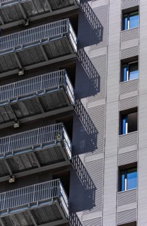 Close-up of a modern urban building facade with metal stairs casting shadows on the wall. The image