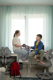 A boy and girl share a moment with a robotic hand. The setting is a cozy, bright room filled with