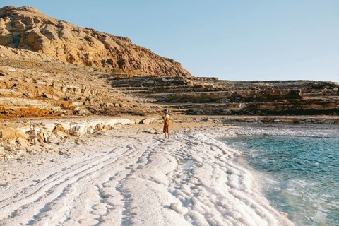 Back view of unrecognizable woman walking alongside the mineral-rich Dead Sea shores in Jordan
