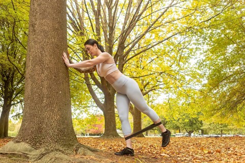 A woman exercises using a resistance band in an autumn park in New Zealand. Surrounded by vibrant