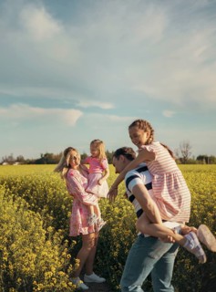 A happy family plays together in a beautiful yellow flower field. The father carries his daughter