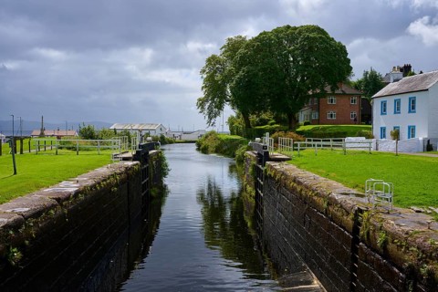 Canal with lock surrounded by lush trees and houses under a cloudy atmosphere, Ardrishaig,