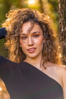 Vertical close-up photo of a young beauty model with curly hair and sensual clothes in the forest