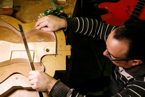 A luthier meticulously shapes a bass guitar body, showcasing the art of craftsmanship. The workshop